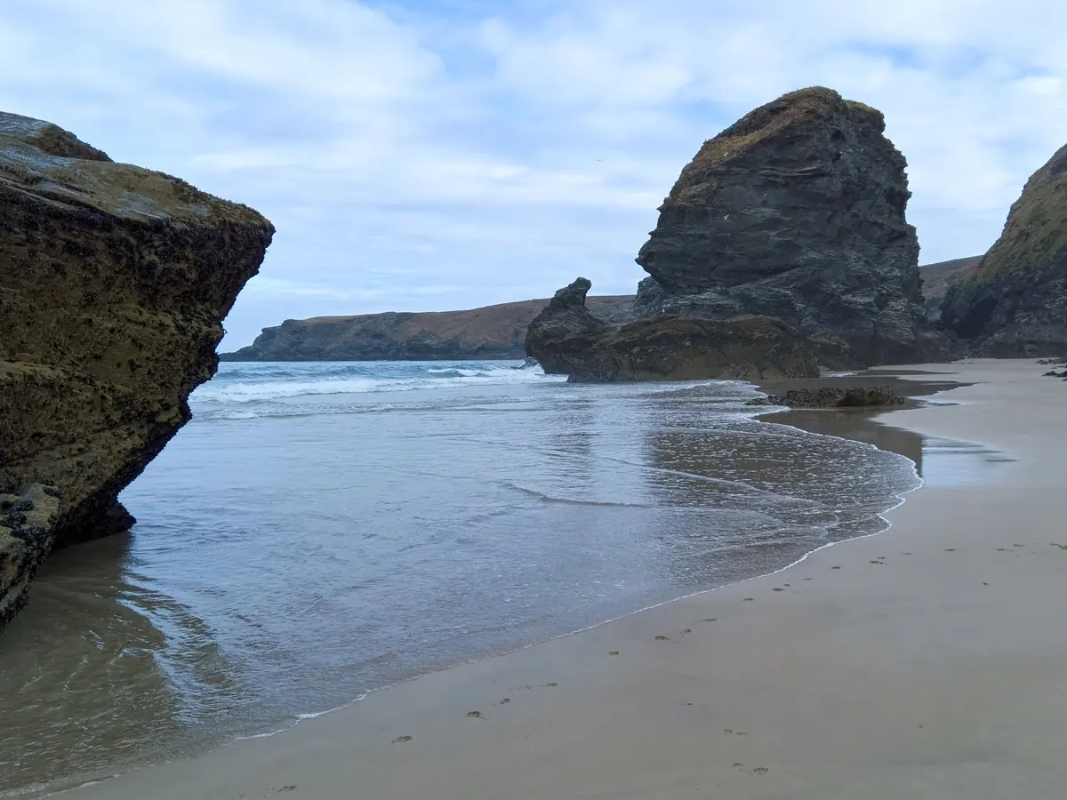 Wet sand reflecting the sky beside tall rock stacks