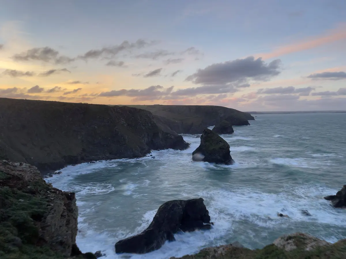 Dark cliffs and sea stacks in rough water at dusk