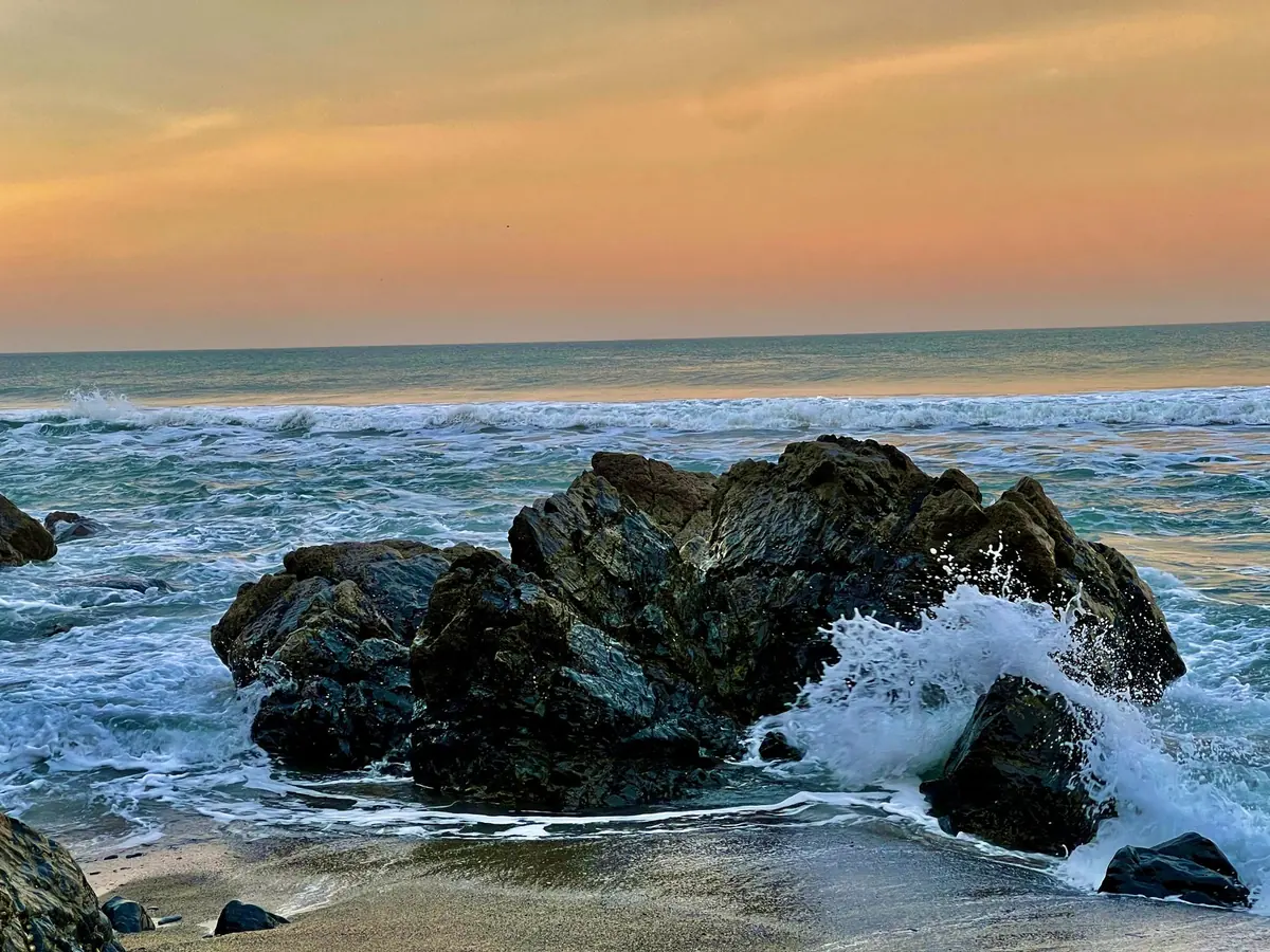 Surf breaking around rocks under an orange sunset sky