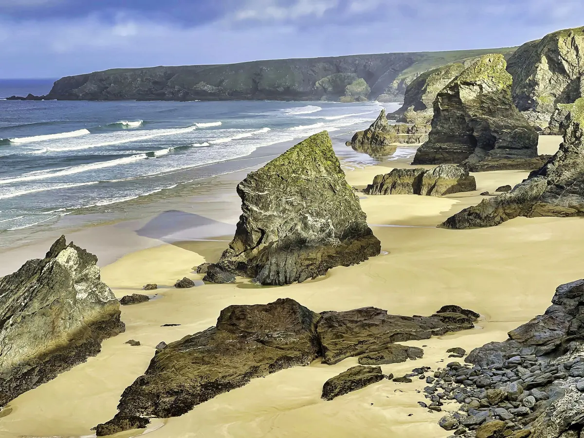 Sea stacks standing on a wide sandy beach with lines of surf beyond