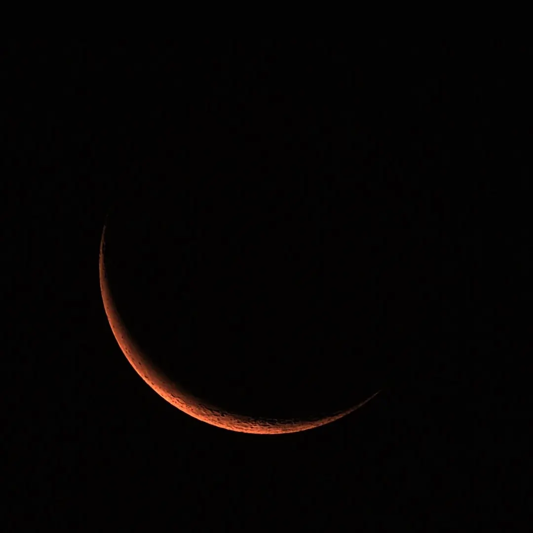 A thin crescent Moon glowing deep orange