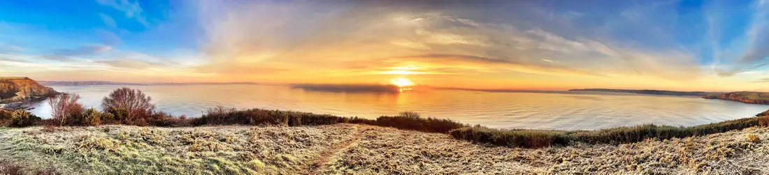 Panorama of a sunrise over a wide bay and frosted headland